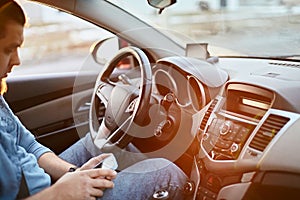 Man driver using mobile phone while sitting at the wheel of a car, sun glare