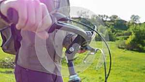 A man drives a bicycle through a green meadow. In the frame you can see his hands and the rudder of a bicycle