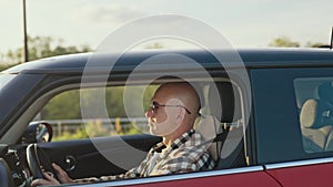 A man drives a car. Bright red car in the setting sun. Traffic in the suburbs.