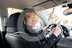 A man driving an Asian car behind the wheel looks at the camera and smiles