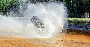 Man driving ATV quad through splashing water with high speed.