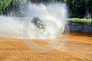 Man driving ATV quad through splashing water with high speed.