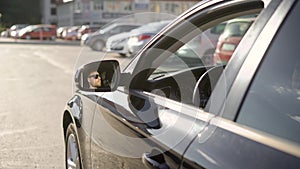 Man is driving big car on city roads, view from outside, his face is reflecting in a rearview mirror in sunny day