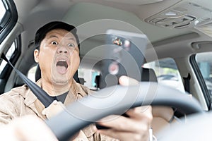 A man is driving a car and looking at his cell phone. He is surprised and excited