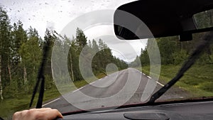 Man driving a car on public road during heavy rainfall with water droplets on windshield and rubber wipers