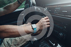 Man driving a car and tuning radio, smart watch on the hand, inside
