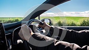 Man driving car. Unrecognizable driver holding hands on steering wheel