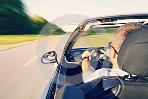 Man driving a convertible car on country road. View from inside behind the driver. man is driving at high speed on the highway.