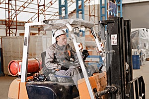 Man driving a forklift through a warehouse in a factory. driver in uniform and protective helmet. the concept of