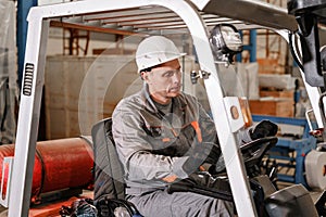 Man driving a forklift through a warehouse in a factory. driver in uniform and protective helmet. the concept of