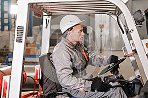 Man driving a forklift through a warehouse in a factory. driver in uniform and protective helmet. the concept of