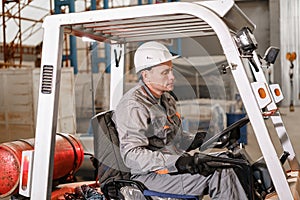 Man driving a forklift through a warehouse in a factory. driver in uniform and protective helmet. the concept of