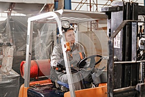 Man driving a forklift through a warehouse in a factory. driver in uniform and protective helmet. the concept of