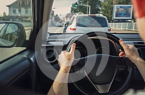 Man driving his car on the city street, close up of person hands on the steering wheel
