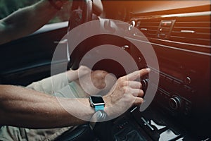 Man driving his car and tuning radio, smart watch on the hand, inside