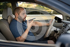 man driving his new car recording the voice message at smartphone, driver using voice command recorder on phone