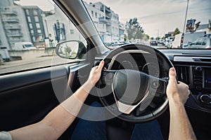 Man driving his new car stands in front of the steering wheel, confident driver on the city streets