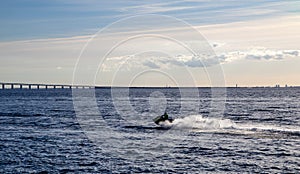 A man driving a jetski on the Oresund strait Ã–resund on a warm summer evening with the Oresund bridge and Copenhagen in the