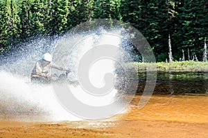 Man driving motocross ATV quad through splashing river lake water with high speed. Foy, Foyross Lake, Sudbury, Canada.