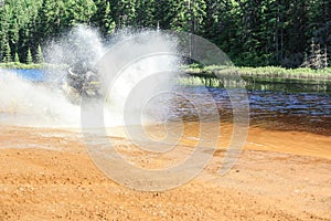 Man driving motocross ATV quad through splashing river lake water with high speed. Foy, Foyross Lake, Sudbury, Canada.