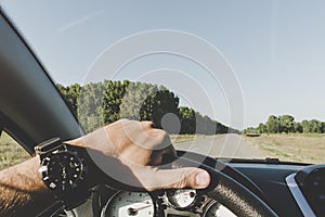 A man is driving on the road outside the city. inside view. man`s hand with with a smart watch on steering the wheel of a car