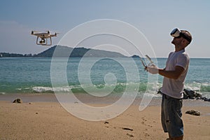 Man with drone camera and virtual reality glasses taking photos and videos on the beach