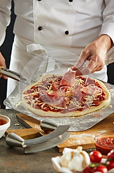 Man dropping sliced meat onto uncooked pizza