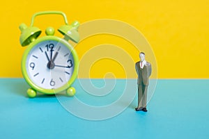 Man dummy next to a green vintage clock on a yellow background.