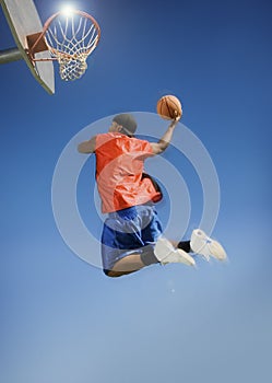 Man Dunking Basketball Into Hoop Against Blue Sky