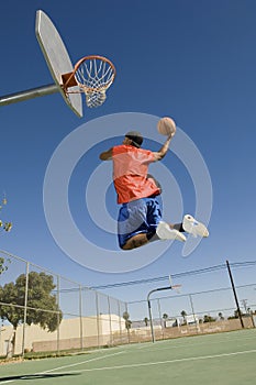 Man Dunking Basketball Into Hoop Against Blue Sky