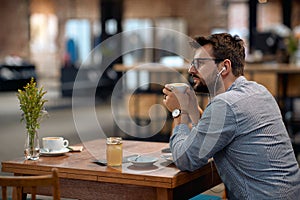 Man with earphones enjoying cup of coffee at cafeteria, sitting alone at table
