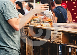 Man eating beef burgers and fries on the street with blurred people in the background