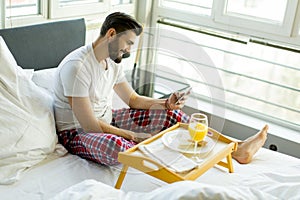 Man eating breakfast in bed whilst using mobile phone
