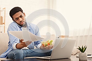 Man eating breakfast, using mobile phone and laptop