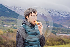 Man eating a bun on the background of Mountains covered with snow and greenery all around