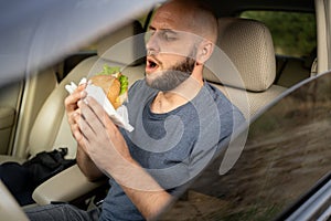 Man eating burger in car. Have a break. Resting in road travel. Dinner In automobile. Front seat. Food concept