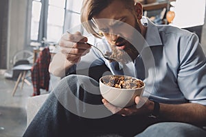 Man eating corn flakes in messy room