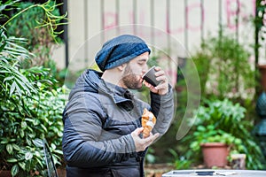 Man eating a croissant and drinking coffee in a garden