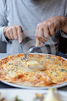 Man eating delicious cheesy pizza in the restaurant with fork and knife