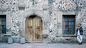 man eating on the facade of a building with wood and stone door, mexico