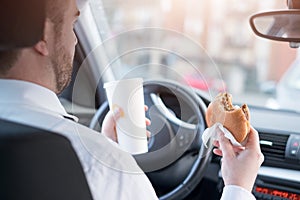 Man eating an hamburger and driving seated in car