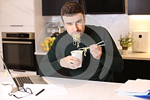 Man eating instant noodles while doing home office work