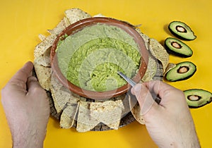 Man eating a Mexican delicious nachos with guacamole on a yellow background