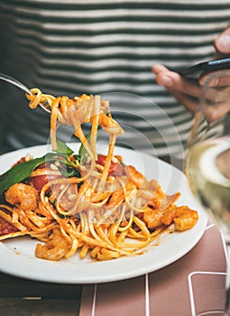 Man eating pasta and looking at smartphone photo