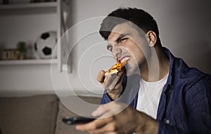 Man eating pizza and holding remote control