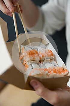 Man eating roll philadelphia with shrimps chopsticks from craft box. delivery service Japanese food rolls in craft box