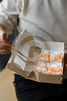 Man eating roll philadelphia with shrimps chopsticks from craft box. delivery service Japanese food rolls in craft box