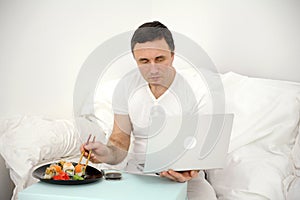 man eating sushi rolls on hotel bed watching film on laptop. caucasian european lady in domestic clothes enjoy having