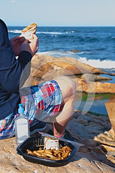 Man is eating takeaway food at the  rocky ocean beach