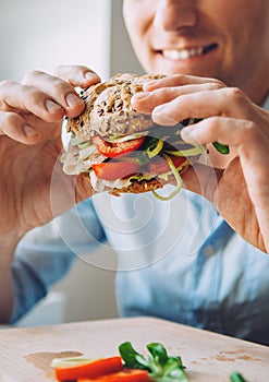 Man eats a big sandwich with meat and vegetables